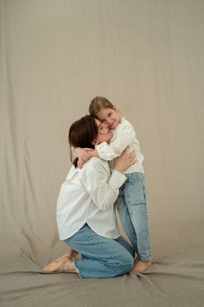 A touching moment between a mother and daughter in a studio setting, both wearing casual outfits.