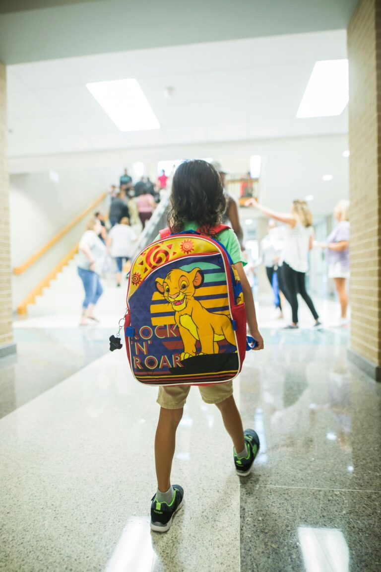 Back view full body schoolkid with backpack walking in crowded corridor of modern building